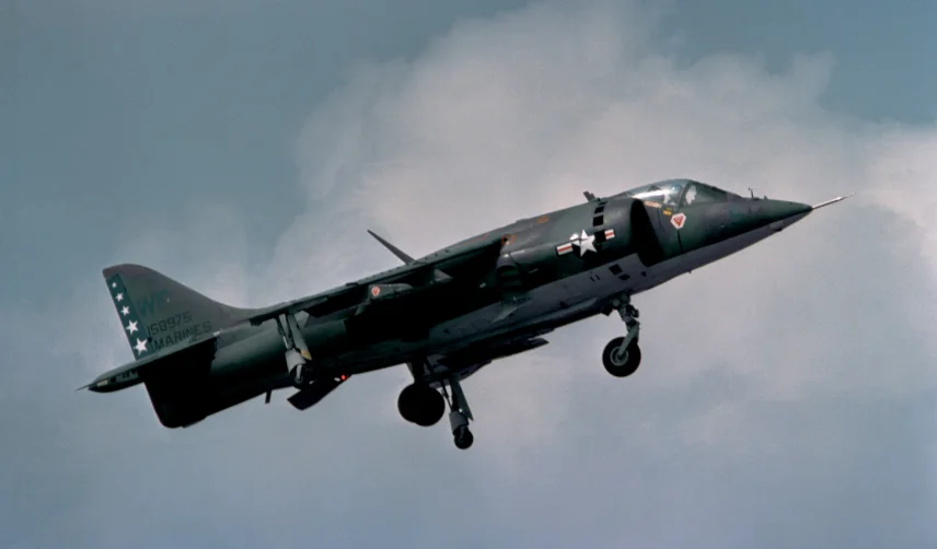A harrier jet flies in a cloudy sky with its landing gear down.